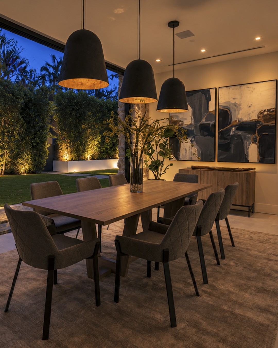 Dining room opening onto a softly lit garden at blue hour